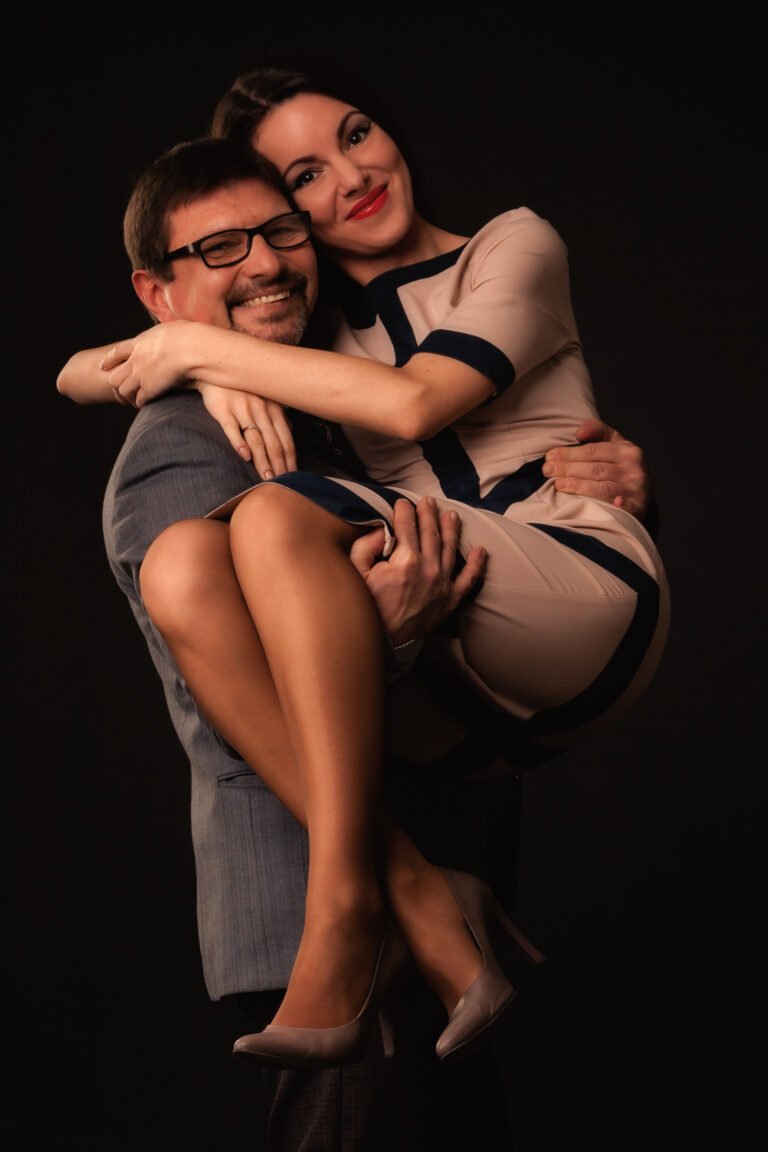 A man is holding a girl in his arms on a dark background